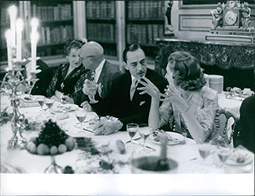 Гроздобер фотографија на грофот и грофицата од Париз што седат на трпезариска маса со луѓе, пиење и разговор, 1959 година.
